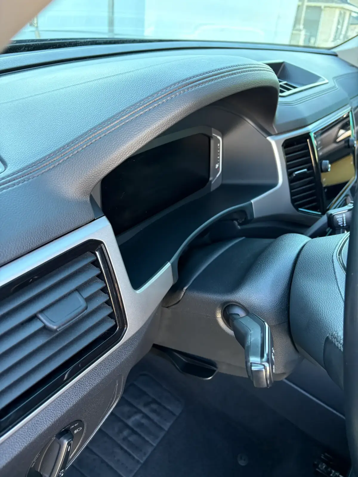 Close-up of a vehicle’s driver-side dashboard, showing stitched trim, a dark instrument display, air vents, part of the steering wheel, and a key in the ignition.