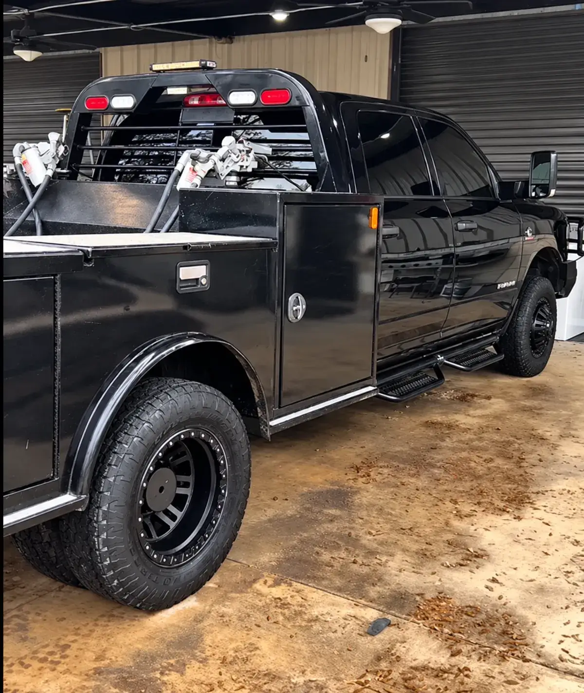 A black utility pickup with side storage compartments, a metal rack, and equipment behind the cab is parked inside a garage.