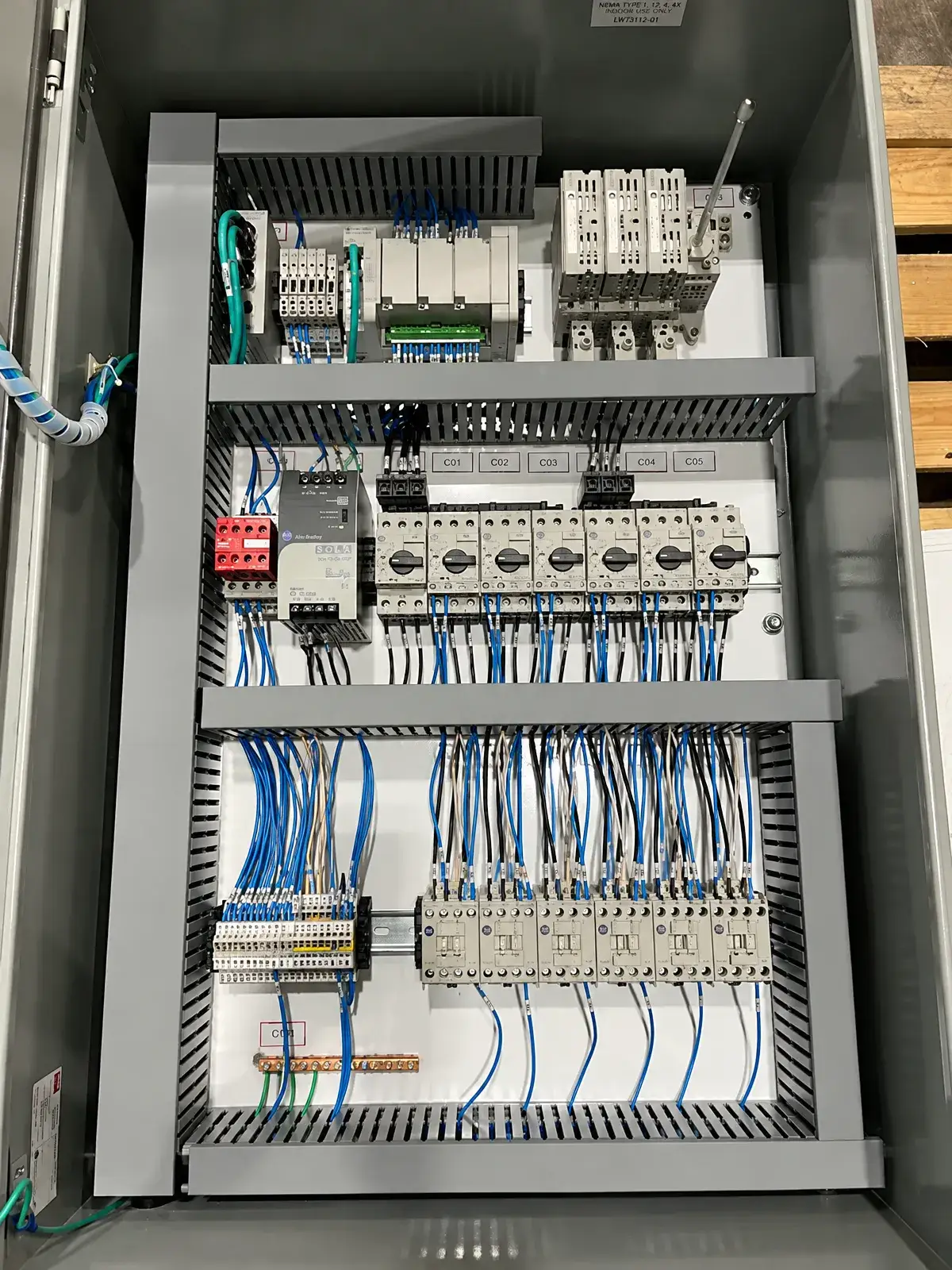 An open electrical control cabinet containing rows of switches, control modules, terminal blocks, and blue and white wiring.